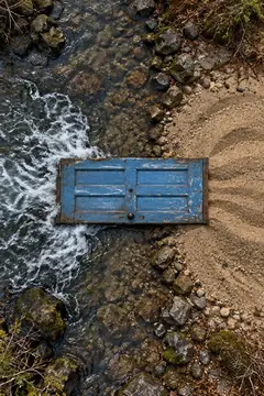 Seen from above, a weathered blue door lies flat where a rushing stream meets a patch of smooth sand, the water stopping neatly at its edge. It doesn't open. It does, apparently, work.