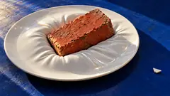 A brick sinks into a white dinner plate that has gone soft as a cushion, on a blue tablecloth. Fine china, finally doing its best.