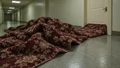 A heap of patterned red hotel carpet spills out from under a closed door into a long tiled corridor, rucked up in folds. There is clearly a lot more of it on the other side.