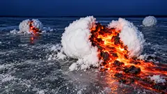 On a frozen lake at dusk, big snowballs have split open to show glowing molten lava inside, spilling across the ice. Nothing is melting.