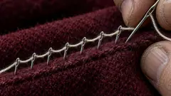 A hand pushes a needle through burgundy wool, but the stitches come out as a row of safety pins. Neat work, if you like being pricked.
